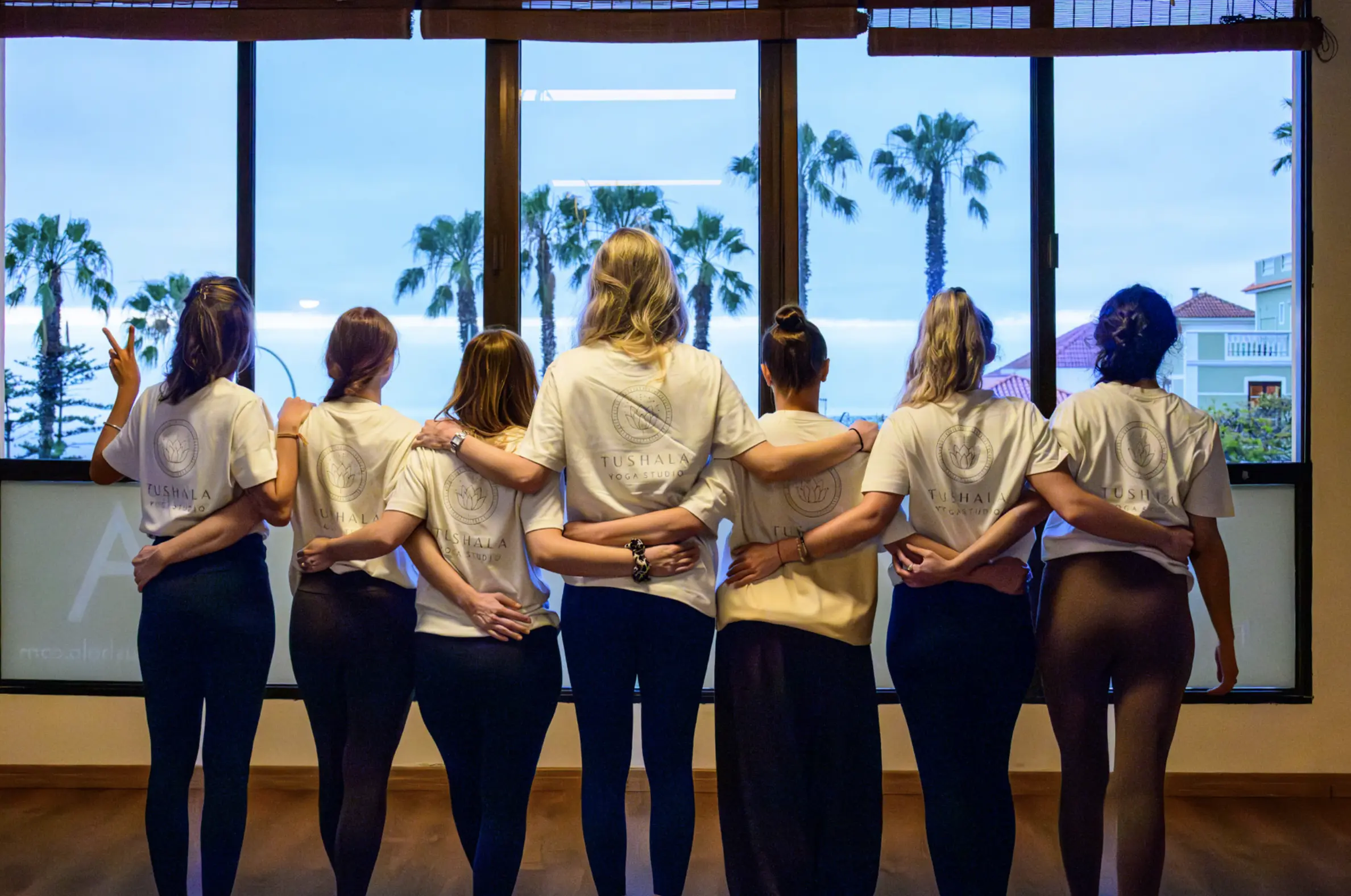 Grupo de alumnas de espaldas, abrazadas, mirando por el ventanal del estudio hacia las palmeras